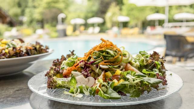 Bunter Salat auf Glasteller mit Wasserbecken im Hintergrund