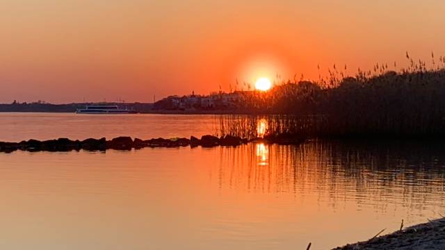 Sicht auf einen See mit orangenem Himmel bei Sonnenuntergang