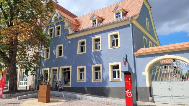 Tourist-Information Bad Lausick in charmantem blauem Gebäude mit Skulptur und Rad-Service – einladender Ort für Gäste mitten in der Stadt.