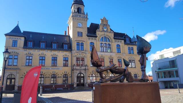 Historisches Rathaus in Bad Lausick mit moderner Skulptur und roter Info-Fahne – einladender Fotopoint am sonnigen Marktplatz.