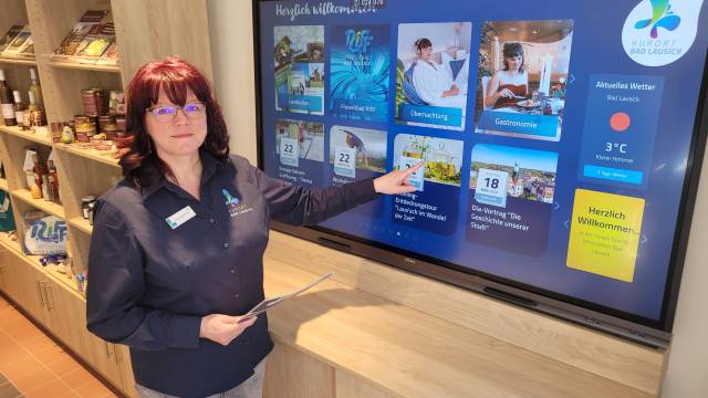 Mitarbeiterin der Tourist-Information Bad Lausick zeigt auf großen Touchscreen mit Infos zu Freizeit, Übernachtung und Veranstaltungen.