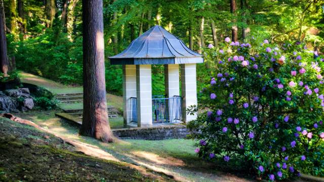 ein kleiner Brunnen mit Pavillon-artiger Überdachung zwischen den Bäumen des Parks