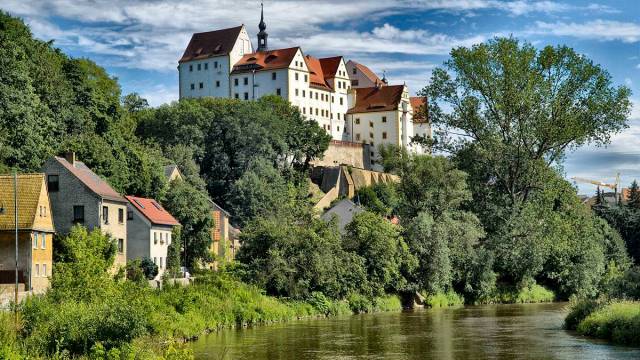Blick von Weitem auf das weiße Schloss Colditz und die Naturlandschaft drum herum